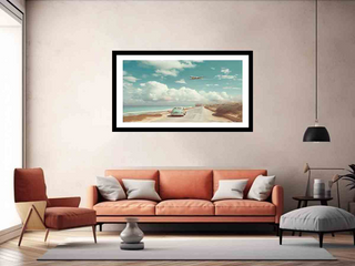 Framed artwork of a beach scene with a car on a road, displayed above an orange sofa in a living room.