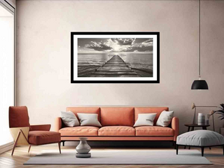 Living room with an orange sofa, armchair, and a framed black and white artwork of a pier.