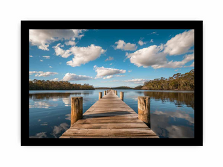 Wooden dock extending into a calm lake with a blue sky and clouds.
