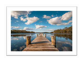 Wooden dock extending into a calm lake with a blue sky and clouds.