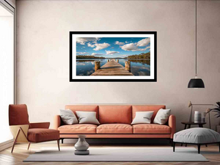 Framed artwork of a dock over water hanging above an orange sofa in a living room.