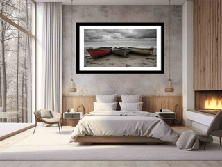 Framed artwork of two boats on a beach above a bed in a bedroom.