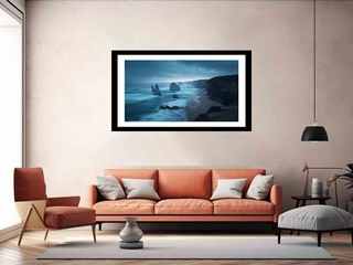 Framed artwork of a coastal scene above an orange sofa in a living room.