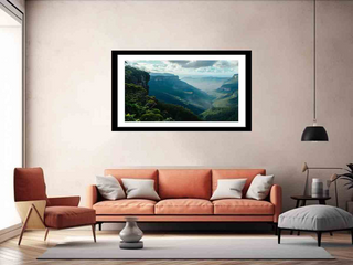Framed landscape print on a wall above an orange sofa in a living room.