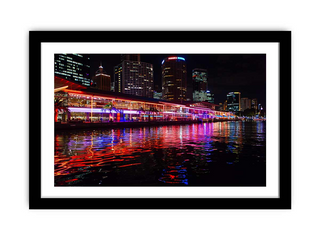 Framed cityscape at night with illuminated buildings and reflections on water.