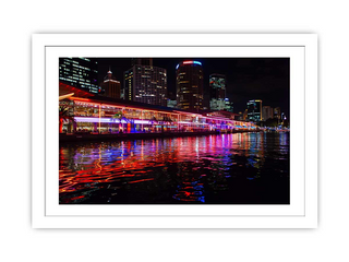 Framed photograph of a city skyline at night with colorful reflections on water.