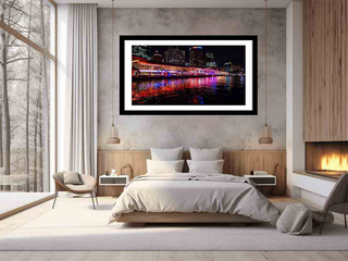 Framed artwork of a cityscape over water on a wall above a bed in a bedroom.