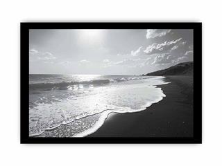 Black and white beach scene with waves and a cloudy sky.