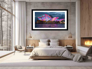 Framed artwork of a colorful building on a wall in a bedroom.