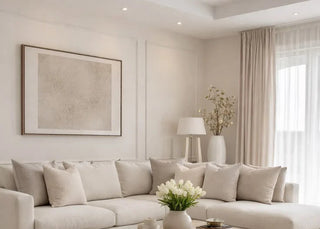 A modern living room featuring a large light beige sectional sofa, a low light-wood coffee table with a vase of white flowers, and a textured cream rug on a light wood floor.